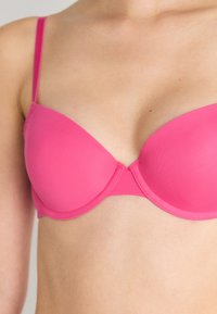 Sutiã acolchoado rosa com alças ajustáveis, copas sem costura e costura delicada nas bordas. Textura suave e acabamento colorido vibrante.