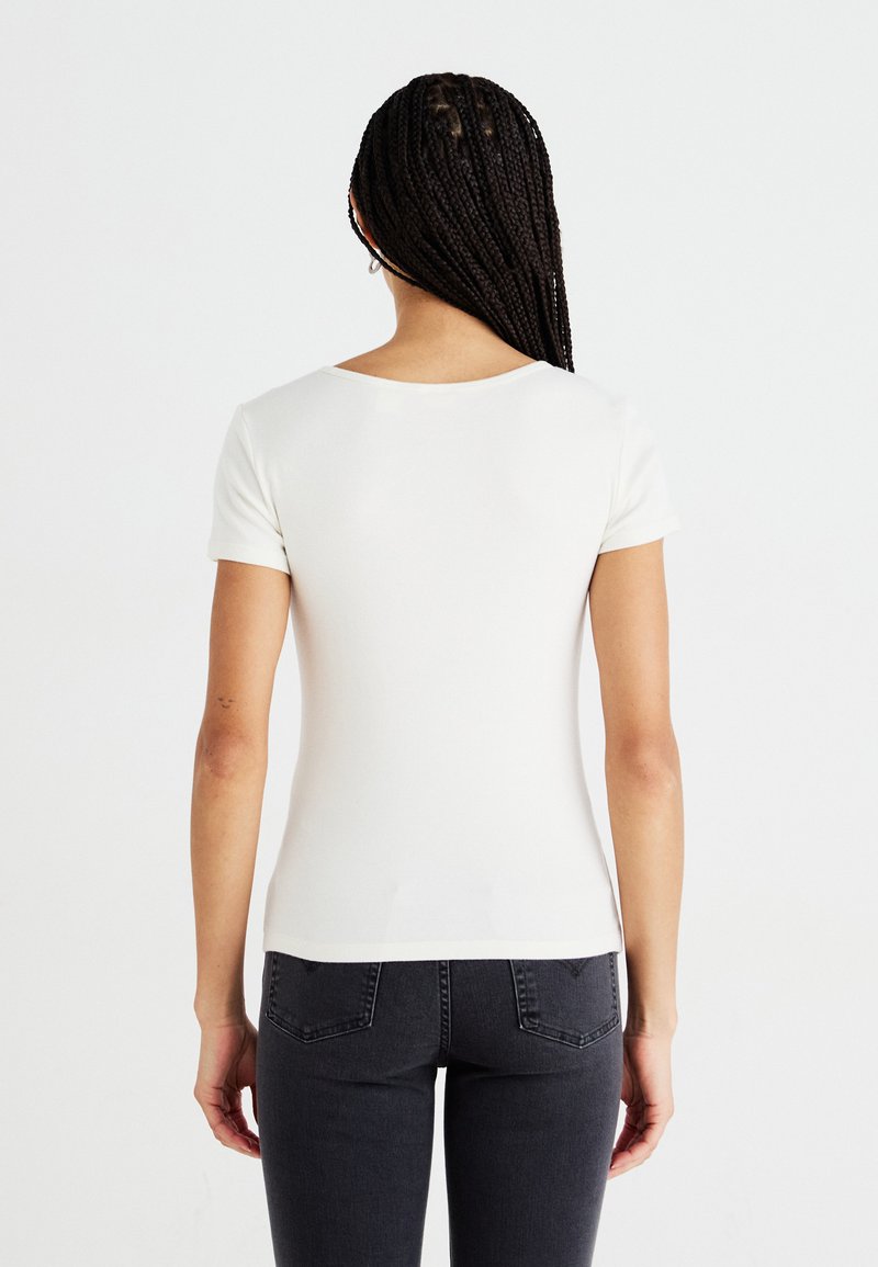 T-shirt blanc à manches courtes avec un col arrondi. Texture lisse, design ajusté et ourlet droit en bas.
