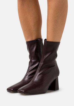 Botines de cuero burdeos con punta cuadrada, silueta cónica y tacón grueso; cuentan con cierre de cremallera y textura fruncida.