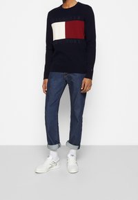 Pull en maille bleu marine avec une texture côtelée et un design en bloc de couleurs comprenant des panneaux blancs et bordeaux. Assorti à un jean bleu retroussé et des baskets blanches.