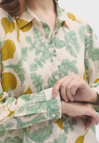 Camicia button-up in tessuto leggero con stampa di verdure verdi e gialle, dotata di colletto e polsini con bottoni.