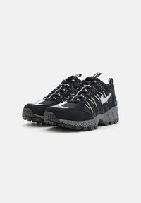 Black athletic shoes with a textured upper, contrasting white accents, and a rugged outsole for traction. Features a lace-up design and pull tab.