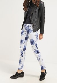 Kalhoty s květinovým vzorem v bílé barvě s modrými květy, spárované s černou koženou bundou a černými slip-on botami. Hladká textura, přiléhavý design.