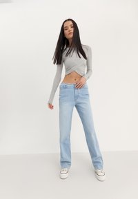 Lys grå langermet cropped topp kombinert med høy midje blå denim jeans. Jeansene har en løs passform og subtil fading, sammen med hvite Sneakers.