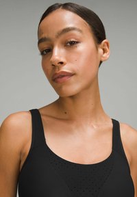 Sujetador deportivo negro con un diseño perforado texturizado en la parte frontal, con tirantes anchos y un ligero escote en V. Textura de tela suave.