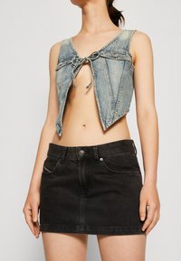 Denim crop top med bindebånd, lys blå farve, ærmeløs design, parret med en sort denim mini-nederdel med forlommer.