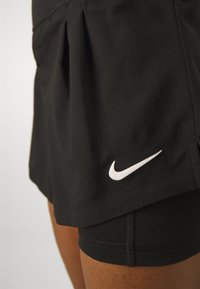Svarta atletiska shorts med en veckad design, prydda med en vit Nike-logotyp. Tillverkade av ett slätt, stretchigt material med ett innerfoder.