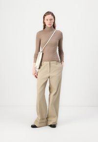 Beige vide benbukser parret med en tætsiddende brun turtleneck. En hvid skuldertaske ligger afslappet. Glat, skræddersyet stoftekstur.