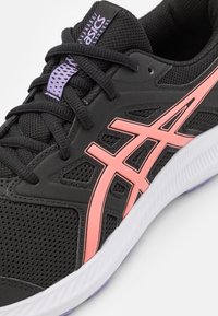 Chaussure de sport noire avec une tige en mesh, rayures roses, surface texturée et une semelle blanche avec des détails violets.