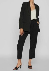Černé sako s výstřihem do klínu, volný střih a boční kapsy. Kombinováno s krémovým tílkem s krajkovým lemem a černými kalhotami na míru.