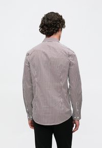 Camisa de rayas con líneas verticales estrechas en rojo y blanco, mangas largas, cuello abotonado y dobladillo curvado. La tela parece suave y ligera.