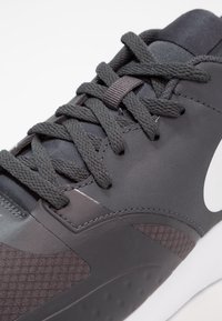 Black athletic shoe featuring textured mesh and smooth synthetic panels, with thick laces and a prominent white logo on the side.
