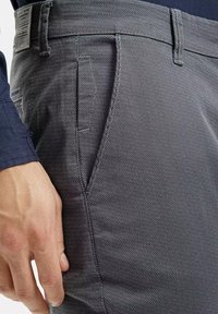 Szare spodnie o fakturze z delikatnym wzorem diamentu, z bocznymi kieszeniami i szlufkami na pasek, wykonane z lekkiego materiału.