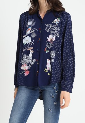 Navy blouse with multicolored bird, flower, mushroom, and dandelion prints, paired with blue jeans featuring embroidered flowers.