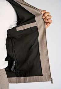 Jasnoszara kurtka z zamkiem błyskawicznym z kontrastową czarną podszewką i wewnętrzną kieszenią. Tkanina ma gładką fakturę z subtelnym wzorem tkania.