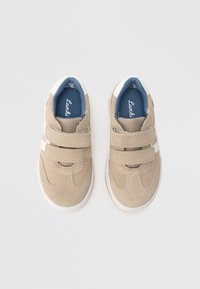 Beige semsket skinnsneakers med hvite detaljer og blått stofffôr. Har to borrelåsstropper og teksturerte såler. Passer til uformell bruk.