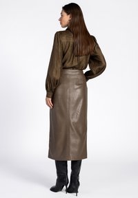 Bruine metallic lange rok gecombineerd met een getextureerde donkerbruine blouse, met pofmouwen en een getailleerde pasvorm. Zwarte kniehoge laarzen maken de look compleet.