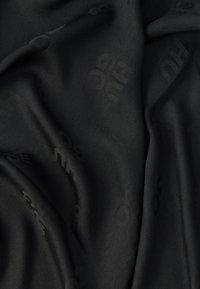 Melns audums ar reljefu rakstu un smalku zīmola veidolu, gluda tekstūra un viegls spīdums, sakārtots mīkstās, viļņveidīgās krokās.