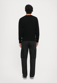 Melna adīta džemperis ar garām piedurknēm, kopā ar melnām kravas biksēm ar sānu kabatām. Abiem ir gluda tekstūra un vienkāršs dizains.