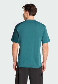 Camiseta atlética en color aqua con cuello redondo, mangas cortas y un corte ajustado. Presenta una tela sutilmente texturizada y un logo en el dobladillo.