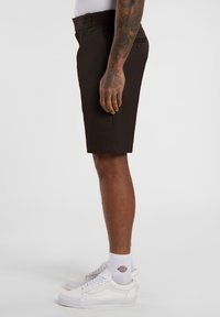 Dark brown shorts with a straight cut, flat front, and belt loops, paired with white sneakers and ribbed socks. Side view.
