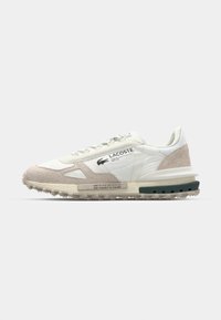Lacoste sneakers met een witte textiele upper, beige suède accenten, gestructureerde zool en logo-detail aan de zijkant. Ronde veters en gewatteerde kraag.