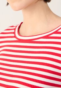 Red and white striped ribbed knit top with a rounded neckline, featuring vertical texture and a fitted design.