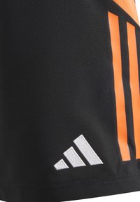 Zwarte sportshorts van synthetisch materiaal met oranje diagonale strepen en een witte geborduurde logo aan de onderkant links.