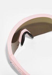 Gafas de sol deportivas rosas con un marco flexible, lentes marrones y una almohadilla nasal de goma negra para mayor comodidad. Presenta el logo en el lateral.