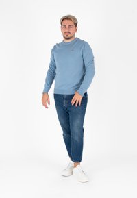 Lichtblauwe gebreide trui met een ronde hals, gecombineerd met donkerblauwe jeans en witte sneakers. Eenvoudig, aansluitend ontwerp met minimale details.