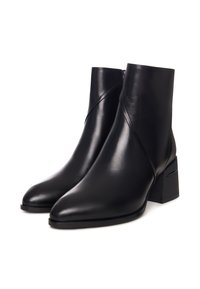 Bottines en cuir noir avec un bout pointu, présentant un design angulaire et un talon carré. Texture lisse et détails minimalistes.