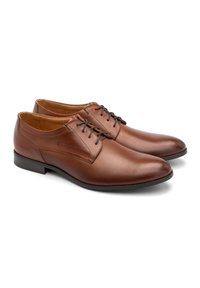 Zapatos de cuero marrón con cordones, de acabado suave, puntera redondeada y suela de goma negra. Presentan acentos en las costuras y un tacón bajo.
