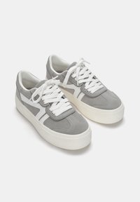 Baskets en suede gris avec semelles en caoutchouc blanc, bout rond, languette rembourrée et bandes latérales blanches contrastées. Elles sont dotées de lacets blancs et d'un intérieur rembourré.