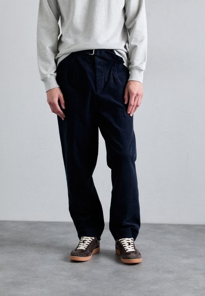 Marineblauwe wijde broek in een relaxte pasvorm, gemaakt van zachte stof, gecombineerd met een lichtgrijze sweatshirt en bruine sneakers met witte veters.
