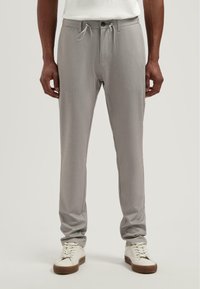 Lichtgrijze broek van een gestructureerde stof met een elastische tailleband, trekkoord en zakken, gecombineerd met witte sneakers.