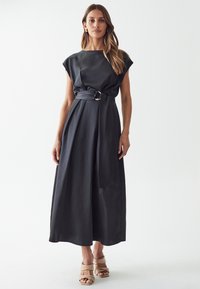 Black satin dress with cap sleeves, a belted waist featuring a circular buckle, and a flowing skirt that reaches the ankles.