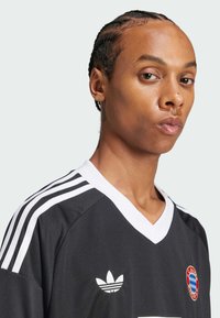 Camiseta atlética negra con acentos blancos, presenta un diseño de cuello en V, tres franjas blancas en los hombros y un logo en el pecho.