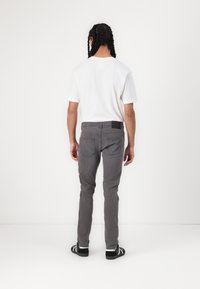 Pantaloni in denim grigio con una vestibilità slim, tasche posteriori e una patch in pelle nera in vita. Abbinati a una t-shirt bianca semplice.