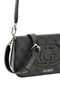 Borsa a mano in tessuto nero con logo impresso, rifiniture in pelle liscia, tracolla regolabile e accessori metallici lucidi. Dettaglio del nome del brand in oro.