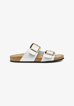 Sandalias blancas de dos correas con hebillas en tono dorado, plantilla de corcho y una suela exterior negra texturizada. Diseño plano con correas ajustables.