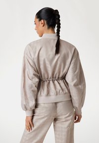 Light gray bomber jacket with a textured pattern, elasticated waistband, and gathered sleeves; smooth fabric with a subtle sheen.