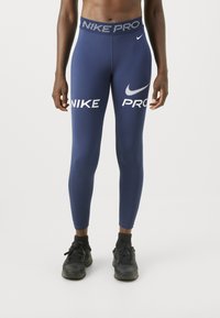 Tengerészkék Nike Pro leggings, márkás elasztikus derékkal és fehér logónyomattal a combon és a lábszáron. Simább, elasztikus anyag.