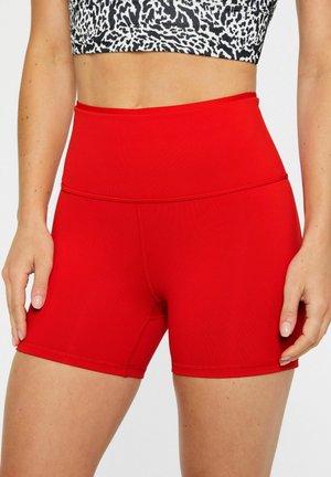 Woman wearing high-waist, bright red athletic shorts and a black-and-white animal print crop top, standing with hands near hips.