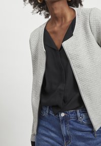 Gray textured zip-up jacket over a black blouse, featuring a round neckline and smooth fabric, paired with blue denim jeans.