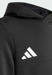 Felpa nera con cappuccio realizzata in tessuto morbido. Presenta un logo Adidas bianco prominente con tre strisce sul davanti.