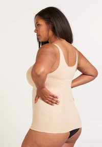 Naadloze huidkleurige tanktop met brede bandjes en geribbeld textuur, die strak rond de taille en heupen aansluit, gecombineerd met zwarte ondergoed.