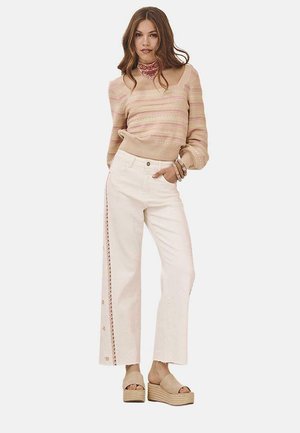 Suéter de punto beige claro con rayas rosas, combinado con pantalones de pierna ancha blancos que presentan botones laterales y un ribete decorativo. Sandalias de cuña beige.