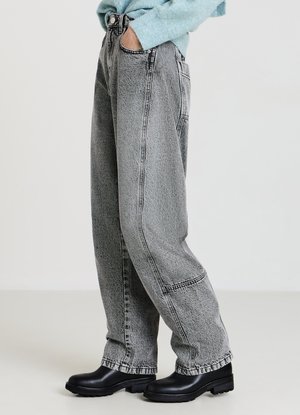 Graue Jeans mit hoher Taille und lockerem Schnitt, mit sichtbaren Nähten, Seitentaschen und kombiniert mit schwarzen Stiefeletten.