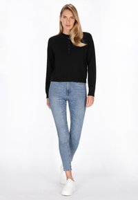 Pulover lung negru cu maneci lungi, decolteu rotund și închidere cu nasture, purtat cu blugi skinny albaștri deschis și adidași albi.