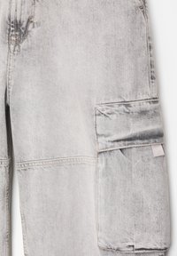 Pantalon cargo en jean gris clair avec grande poche latérale dotée d'un rabat et de détails de couture visibles.